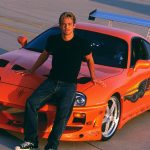 Paul Walker sobre el capo de su toyota supra naranja.