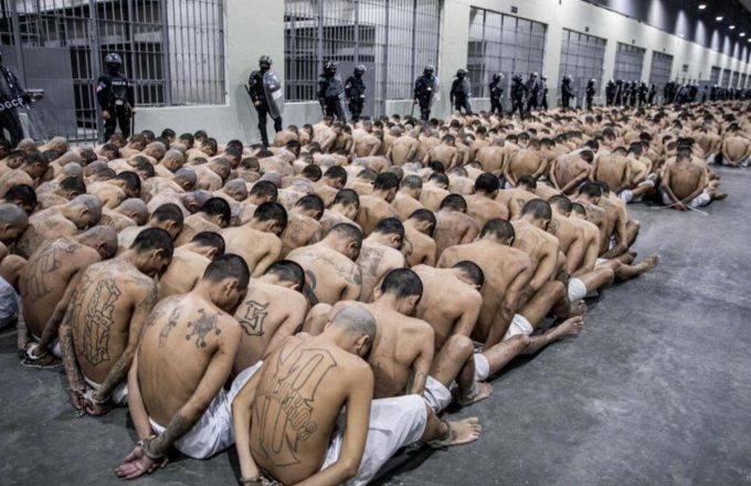 Muchos reclusos sentados en el suelo de una cárcel, solo vistiendo una pantaloneta corta y rapados por completo
