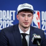 La joven promesa sentada en una silla en el NBA DRAFT luciendo una gorra de loa Dallas Mavericks