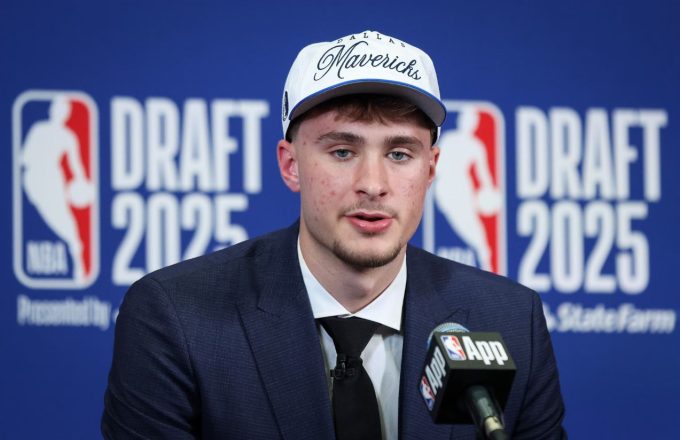 La joven promesa sentada en una silla en el NBA DRAFT luciendo una gorra de loa Dallas Mavericks