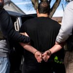 Dos policias tomando por el brazo a una persona mientras la misma está esposada