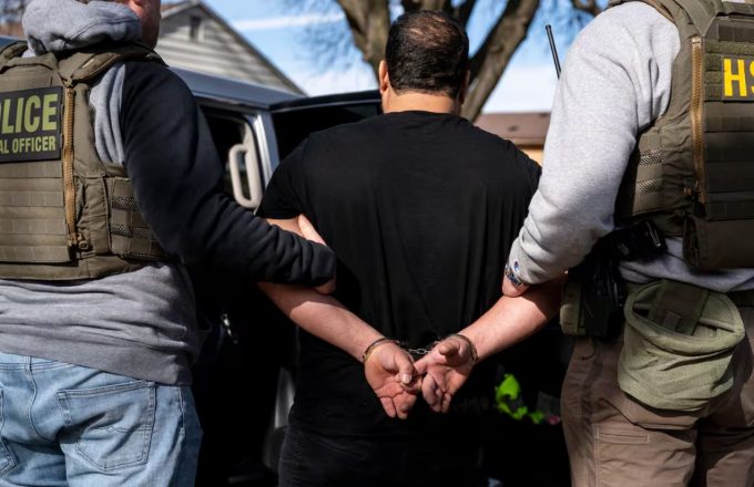 Dos policias tomando por el brazo a una persona mientras la misma está esposada