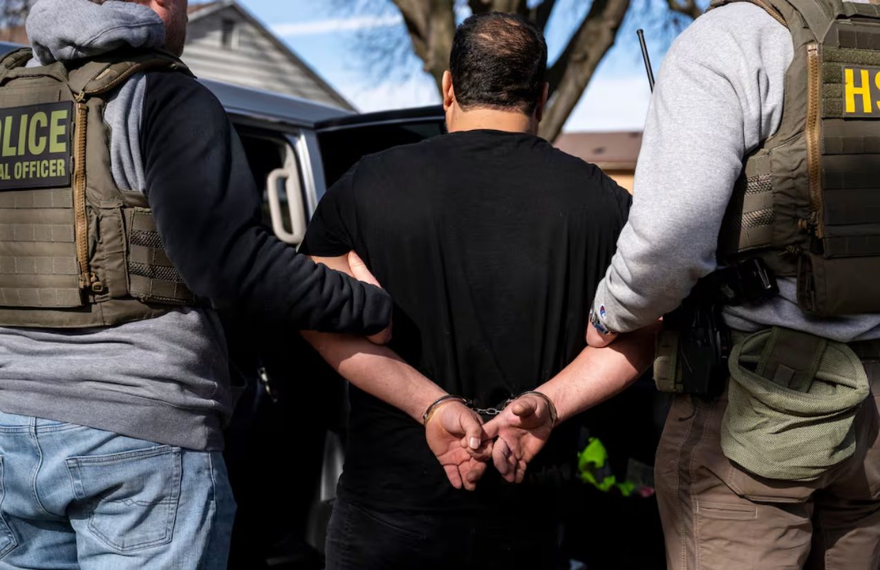 Dos policias tomando por el brazo a una persona mientras la misma está esposada
