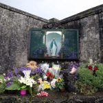 Un muro con muy viejo con una virgen en medio y muchas flores por debajo de la misma
