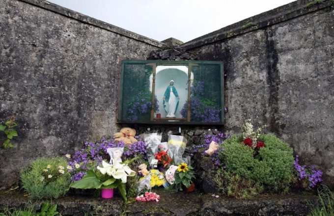 Un muro con muy viejo con una virgen en medio y muchas flores por debajo de la misma