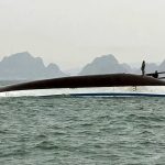 Un barco boca abajo con algunas personas tratando de subirse a la base para no ahogarse