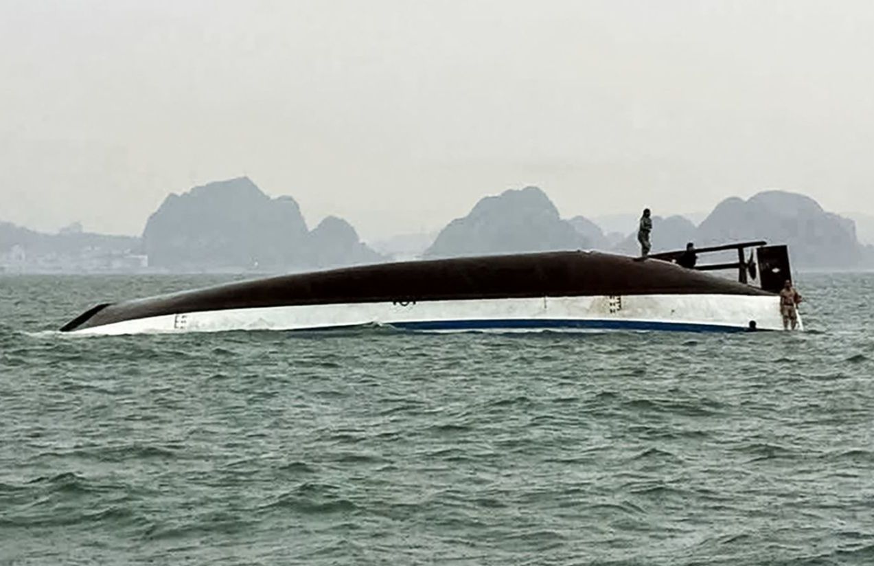 Un barco boca abajo con algunas personas tratando de subirse a la base para no ahogarse