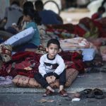 Un niño sentado en un andén de la calle con mucha ropa y trapos sucios a sus espaldas