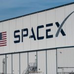 Un almacen grande en color blanco con la palabra SPACEX y la bandera de Estados Unidos a un lado