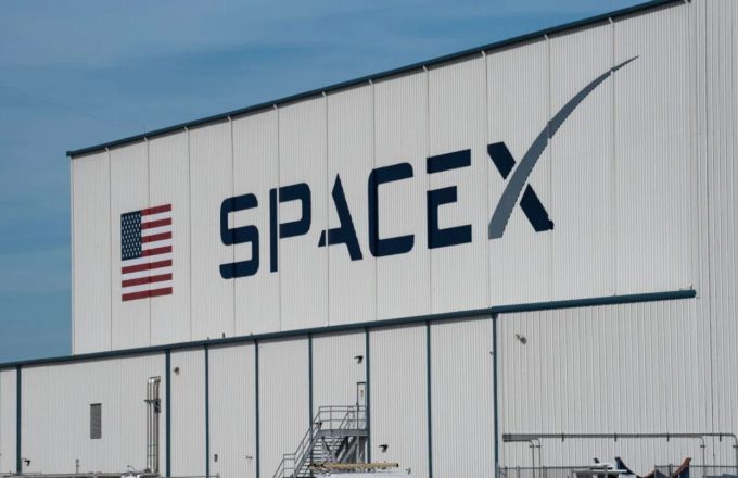 Un almacen grande en color blanco con la palabra SPACEX y la bandera de Estados Unidos a un lado