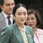 La primera ministra de Tailandia con un traje color verde y detrás varias personas