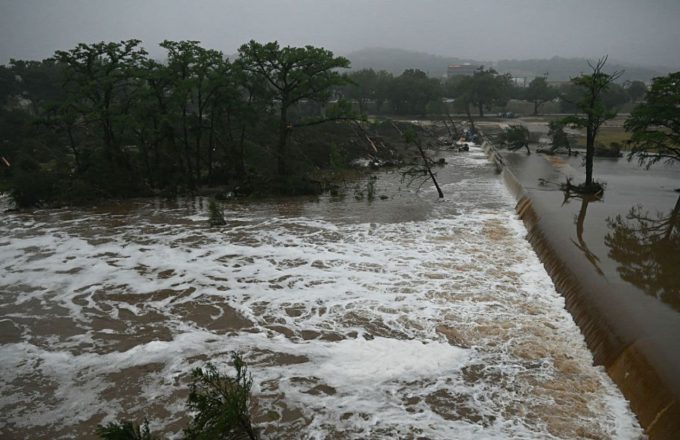 A large river overflowing and sweeping away trees and everything in its path