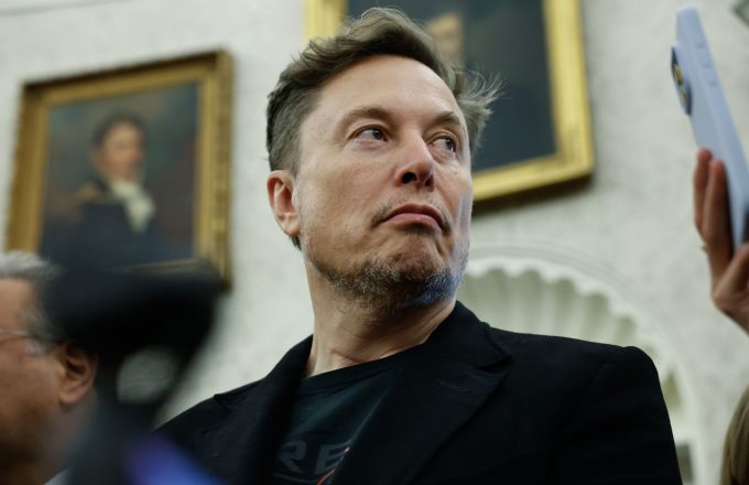 Elon Musk looking to the side while wearing a neat black suit
