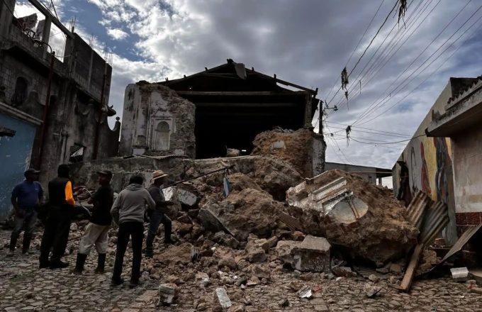 A house torn to pieces, with several people watching and searching for the injured