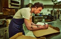 A chef in the middle of his workplace writing something on a piece of cardboard